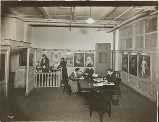 Hauptbüro/Empfangsraum bei der Mutual Film Co. mit Sekretärin am Schreibtisch, Menschen an einem Tisch beim Lesen und Porträts an der Wand, New York
