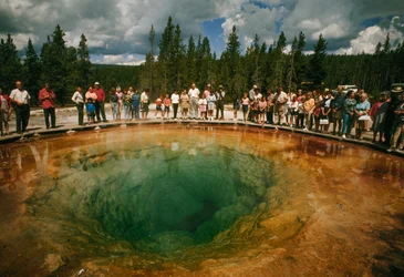 Parkbesucher versammeln sich um einen blau-grünen, blütenförmigen Thermalpool. Yellowstone Nati...