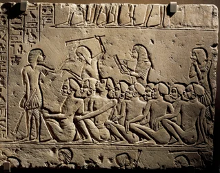 Eine Gruppe Schwarzer Gefangener, umringt von mit Keulen bewaffneten Wachen, während ein Schreiber einen Bericht anfertigt, Relief aus dem Grab des Haremhab in Sakkara