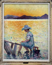 Saint Tropez, Sonnenuntergang. Eine Frau sitzt mit ihren Füßen im Wasser am Ufer