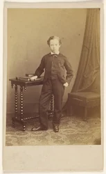 [Unidentifizierter kleiner Junge im Anzug an einem Tisch mit Büchern]