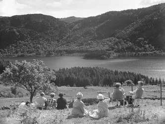Gruppe von Menschen sitzt auf Gras oder Liegestühlen und schaut auf eine Aussicht von Thirlmere