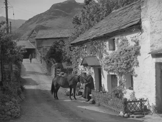Alte Dame streichelt Pferd, das auf der Straße vor Cottage steht
