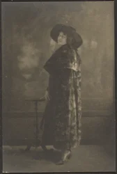 [Porträt einer Frau im langen Mantel vor Wandteppich]