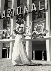 Modell im Hochzeitskleid des Modehauses "Lamma". Der Artikel zeichnet sich durch einen Kopfschmuck im klösterlichen Stil aus, der am Hals mit einer auffälligen Traubenbrosche gehalten wird.