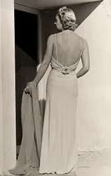 Modell von hinten gesehen trägt Abendkleid des Modehauses "Fumach". Der Artikel lässt den Rücken frei und ist mit einer juwelenbesetzten Brosche verziert.