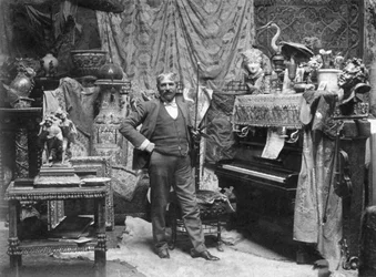 Ganzkörperporträt des Malers Francesco Vinea im Atelier von Donatello in Florenz. Er posiert in einem Raum, der mit zahlreichen Vorhängen, chinesischen Vasen, kleinen Skulpturen und Nippes dekoriert ist. Rechts ein Klavier und eine Geige (s/w Foto)