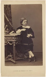 [Unidentifiziertes kleines Mädchen, das mit dem Ellbogen auf einem geschlossenen Buch auf einem Tisch steht]