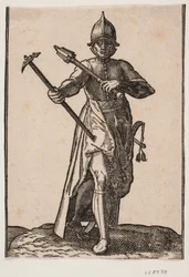 Stehender Soldat mit Helm, frontal gesehen; in der rechten Hand ein Kriegshammer, in der linken Hand eine Keule, das hintere Bein und der Fuß verdreht im Verhältnis zum vorderen; an der linken Seite ein Schwert
