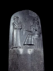 Mesopotamien: Stele aus Diorit mit dem Gesetzescode von Hammurabi. Sie ist mit Keilschriftinschriften bedeckt und oben steht König Hammurabi vor dem Sonnengott Mesopotamiens, Shamash, der Gottheit der Gerechtigkeit