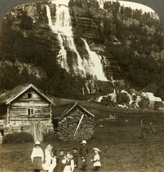 Kinder spielen auf einem Bauernfeld mit terrassiertem Tvinde-Wasserfall, Vossevangen, Norwegen