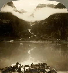 Grytereids-Gletscher, der über treibenden Wolken über dem ruhigen See Olden, Norwegen, glitzert