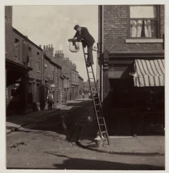 Mann reinigt eine Gaslaterne, um 1905