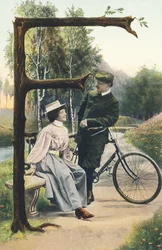 F: Ein Mann in Radfahrerkleidung lehnt an seinem Fahrrad und unterhält sich mit einer Frau, die auf einer Bank sitzt. Ländliche Umgebung - Alphabet Figuren Ref Th. E., L. Theochrom - Serie 994. Theodor Eisman, Verleger, Leipzig