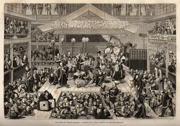Eine Bühne des japanischen Theaters in Yokohama, mit drei Galerien für die Zuschauer; die Schauspieler spielen auf einer hohen Bühne, jeder begleitet von einem Mann, der einen langen Stock hält, an dessen Ende eine Kerze befestigt ist; während der Aufführu