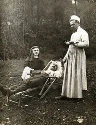 Arzt misst den Puls eines verletzten Mannes, assistiert von einer Krankenschwester-Nonne, ca. 1900